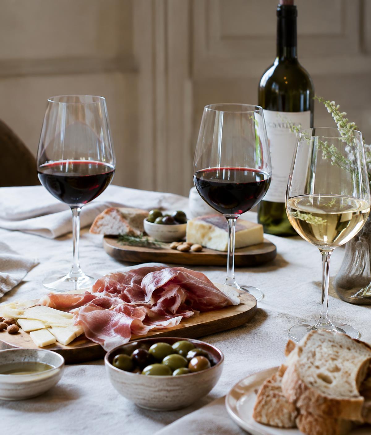 Wine glasses with cheese, prosciutto and olives on a linen table